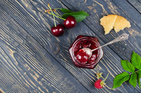 Cherry jam and raspberry in glass jars on wooden table. Top view