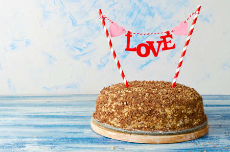 Festive cake with a topper Love on a blue background. Honey cake with walnuts and grated chocolate