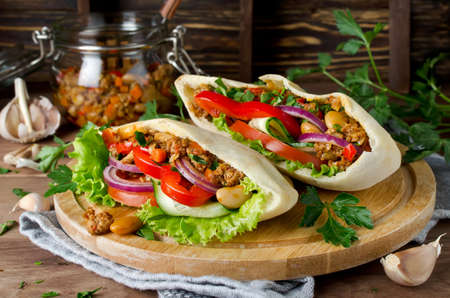 Pita bread sandwiches with meat, beans and vegetables. Served on wooden cutting boardの写真素材