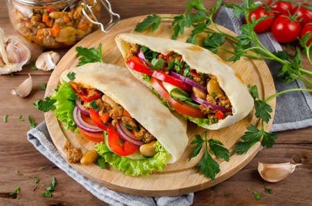 Pita bread sandwiches with meat, beans and vegetables. Served on wooden cutting boardの写真素材