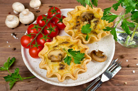 Baked homemade quiche pie in mini metal forms served with fresh greens, on a plate on old plank wooden backgroundの写真素材