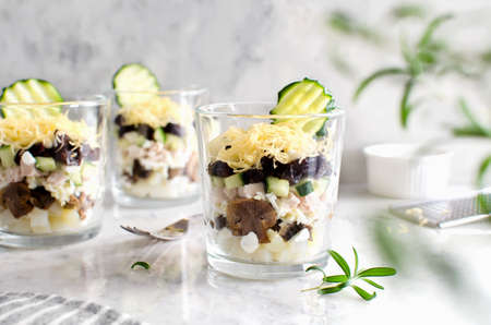 Layered salad with chicken, mushrooms, prunes, eggs, cucumbers, potatoes and cheese. Salad in a...