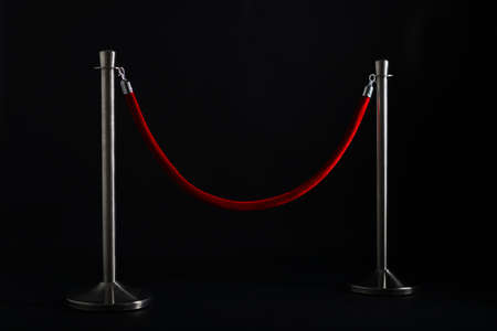 silver stanchions with a red rope, isolated on blackの写真素材