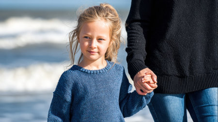 Cute little girl and her mother walking on the beach at autumn dayの素材