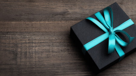 Black gift box with blue ribbon bow on wooden background, top viewの素材