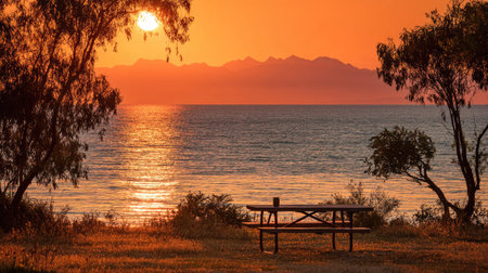 Sunset over the sea with a bench in the foreground and mountains in the backgroundの素材