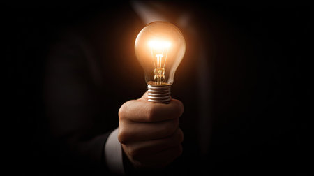Close up of businessman hand holding light bulb on dark background. Idea conceptの素材