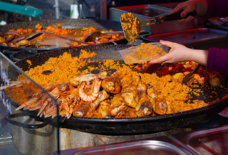 Paella being scooped into serving dish from a large pan at a farmers marketの写真素材