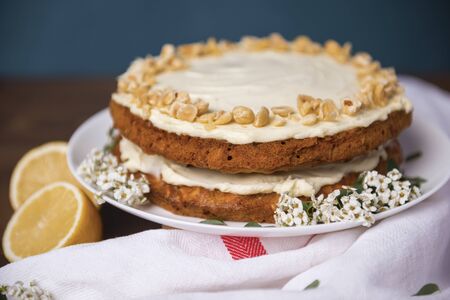 Carrot cake with hazel nuts, decorated with white flowers of meadowsweet and slice lemon on the wooden table, pie cooked with carrot biscuit and sour cream, decorated with hazel nutsの写真素材