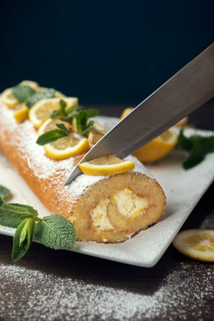 Lemon roll cake decorated with slices of lemon fruit and leaves of mint, lemon pie with butter cream on the white plateの写真素材