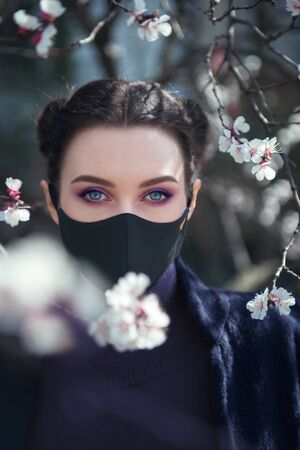 Close-up portrait of young pretty girl with the protective mask with blooming trees on the backgroundの写真素材