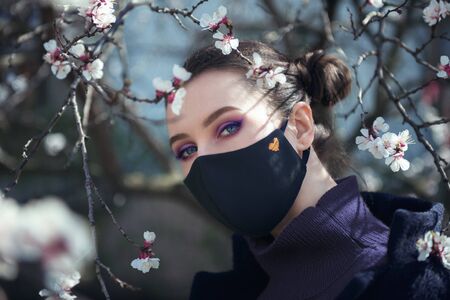 Close-up portrait of young pretty girl with the protective mask with blooming trees on the backgroundの写真素材