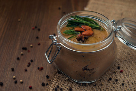 Glass jar with poultry pate, decorated with almonds and rosemary on the sackcloth and wooden background, homemade liver paste decorated with spices on the burlap wooden tableの写真素材
