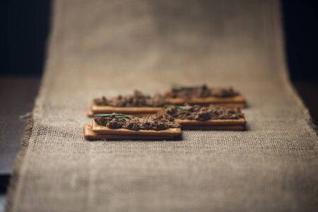 A few crackers with poultry pate on the sackcloth and wooden background, homemade liver paste decorated with spices on the burlap wooden tableの写真素材