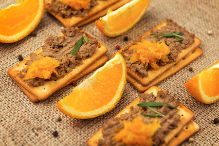 A few crackers with poultry liver pate and orange jam, slice of orange fruits on the sackcloth...