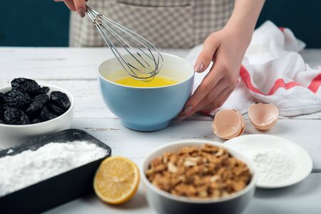 Female hands beat egg whites. Ingredients for merengue roll cooking. Baking or cooking on white wooden background with ingredients.の写真素材