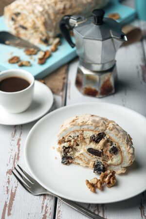 A cup of coffee and meringue roll on a white vintage wooden kitchen table with burlap napkin. Meringue pie decorated with prunes and walnuts on blue cutting board.の写真素材