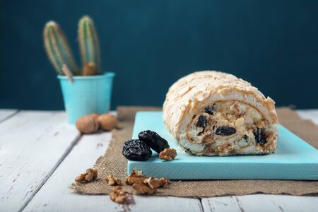 Meringue roll on a white vintage wooden kitchen table with burlap napkin. Meringue pie decorated with prunes and walnuts on blue cutting board.の写真素材
