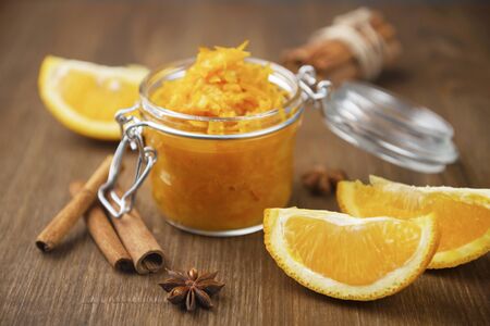 A jar of orange confiture with slices of orange fruit, cinnamon and star anise on the wooden background, homemade orange jam with the few pieces of bread on the wooden tableの写真素材