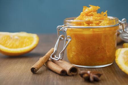 A jar of orange confiture with slices of orange fruit, cinnamon and star anise on the wooden background, homemade orange jam on the wooden tableの写真素材