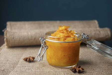 A jar of orange confiture with star anise on the sackcloth and wooden background, homemade orange jam with the few pieces of bread on the burlap wooden tableの写真素材