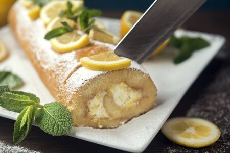 Lemon roll cake decorated with slices of lemon fruit and leaves of mint, lemon pie with butter cream on the white plateの写真素材