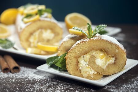 Lemon roll cake decorated with slices of lemon fruit and leaves of mint, lemon pie with butter cream on the white plateの写真素材