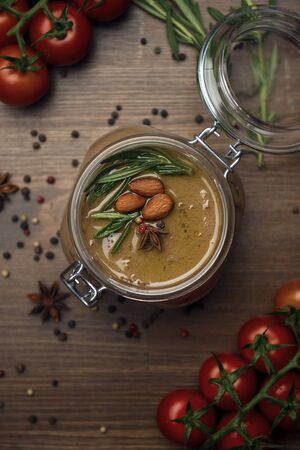 Glass jar with poultry pate, decorated with almonds and rosemary with cocktail tomatoes on a wooden table, homemade liver paste decorated with spicesの写真素材