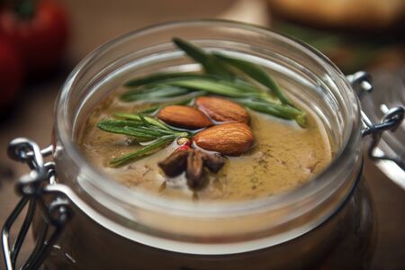 Close-up glass jar with poultry pate, decorated with almonds and rosemary with cocktail tomatoes on a wooden table, homemade liver paste decorated with spicesの写真素材