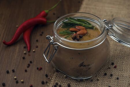 Glass jar with poultry pate, decorated with almonds and rosemary and red hot peppers on the sackcloth and wooden background, homemade liver paste decorated with spices on the burlap wooden tableの写真素材