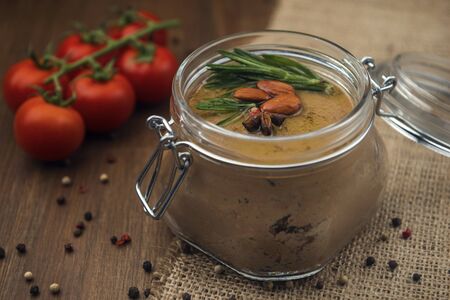 Glass jar with poultry pate, decorated with almonds and rosemary and red cocktail tomatoes on the sackcloth and wooden background, homemade liver paste decorated with spices on the burlap wooden tableの写真素材