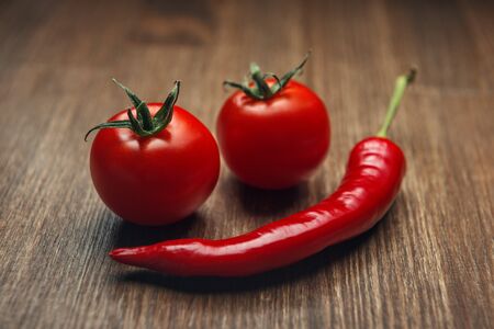 Red ripe fruits of chili pepper and cherry tomato on a wooden tableの写真素材