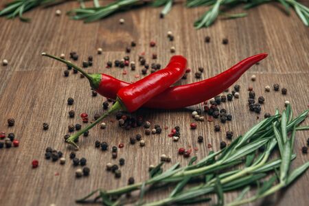 Red ripe fruits of chili pepper with peppercorns and rosemary on a wooden backgroundの写真素材