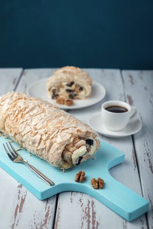 A cup of coffee meringue roll on a white vintage wooden kitchen table. Meringue pie decorated with prunes and walnuts on blue cutting board.の写真素材