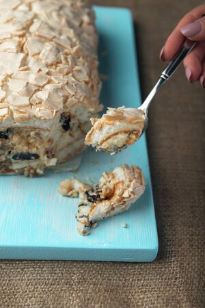 A piece of meringue roll and meringue roll on a white vintage wooden kitchen table with burlap napkin. Meringue pie decorated with prunes and walnuts on blue cutting board.の写真素材