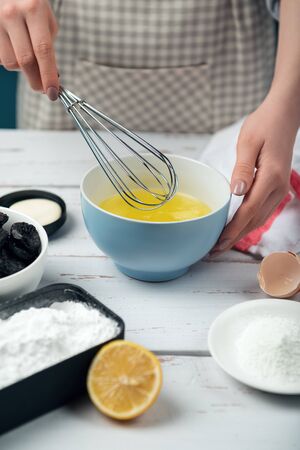 Female hands beat egg whites. Ingredients for merengue roll cooking. Baking or cooking on white wooden background with ingredients.の写真素材