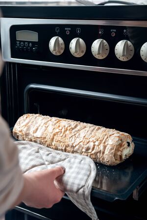 A woman takes out a meringue roll from an electric oven. The process of making meringue roll.の写真素材
