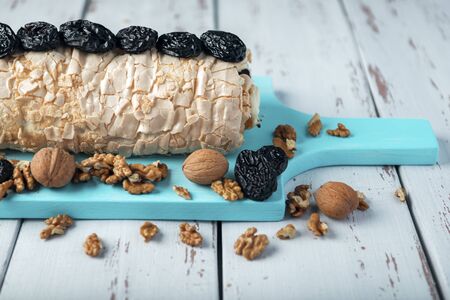 Prune-nut meringue roll on a blue cutting board on a white vintage wooden kitchen table. Meringue pie decorated with prunes and walnuts.の写真素材