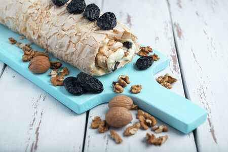 Prune-nut meringue roll on a blue cutting board on a white vintage wooden kitchen table. Meringue pie decorated with prunes and walnuts.の写真素材