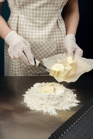 Cook placing small pieces of butter into flour on kitchen table from stainless steel. Safely cooking process of tart, cookies or bakery. Gloved hands.の写真素材