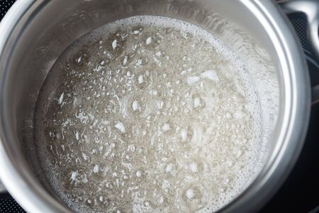 Boiling sugar syrup in a stainless steel pan. Boiling transparent liquid in a metal containerの写真素材
