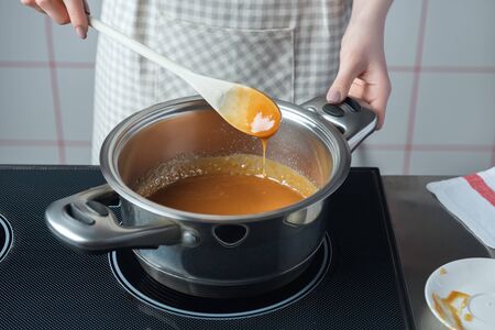 Women in checkered apron with wooden spoon preparing caramel in the stainless steel pan.の写真素材