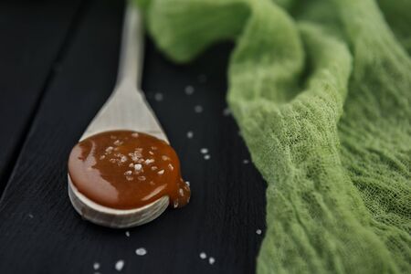 Wooden spoon with homemade salted caramel, crystals of sea salt and green gauze on black wooden tableの写真素材