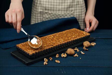 Woman in checkered apron filling pie shell with nuts and salted caramel. Process of making a tart.の写真素材