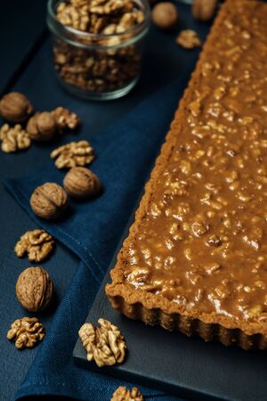 Walnut-caramel tart on a black serving board with walnuts on dark wooden table.の写真素材