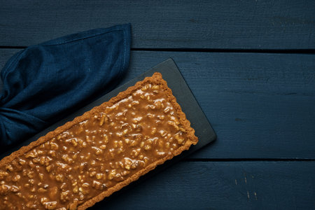Walnut-caramel tart on a black serving board on dark wooden table. Top view. Space for text.の写真素材