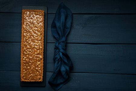 Walnut-caramel tart on a black serving board on dark wooden table. Top view. Space for text.の写真素材