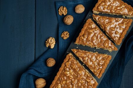 Chopped walnut-caramel tart on a black serving board with walnuts on dark wooden table. Top view. Space for text.の写真素材