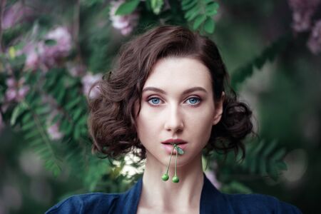 Young beautiful dreamy girl with green cherries on a background of blooming acacia. Outdoor portrait of a romantic woman.の写真素材