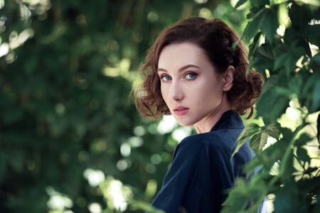 Young beautiful dreamy girl on a background of green leaves. Outdoor portrait of a romantic woman.の写真素材